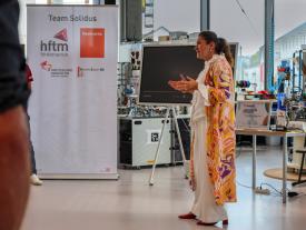 Frau in farbenfroher Kleidung hält eine Rede bei Team Solidus/hftm Veranstaltung