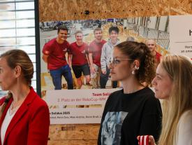 Drei Frauen stehen vor einem Team Solidus Poster.